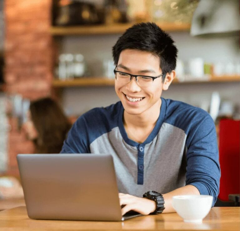 a man happily using a laptop in a cafe