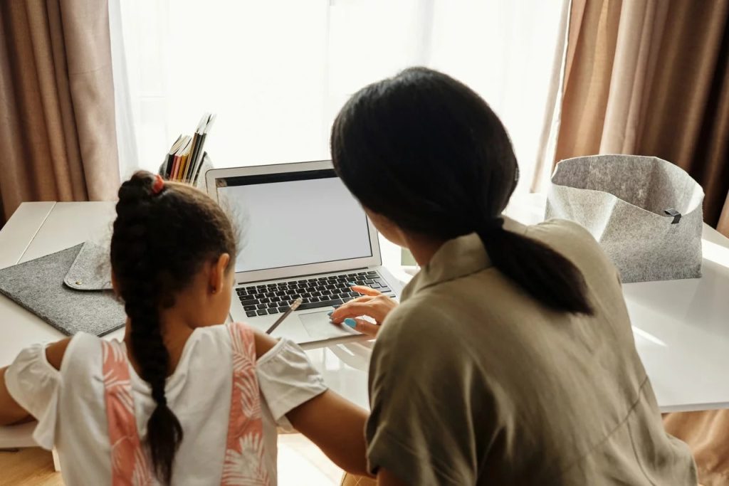 a mother on a laptop helping her daughter study